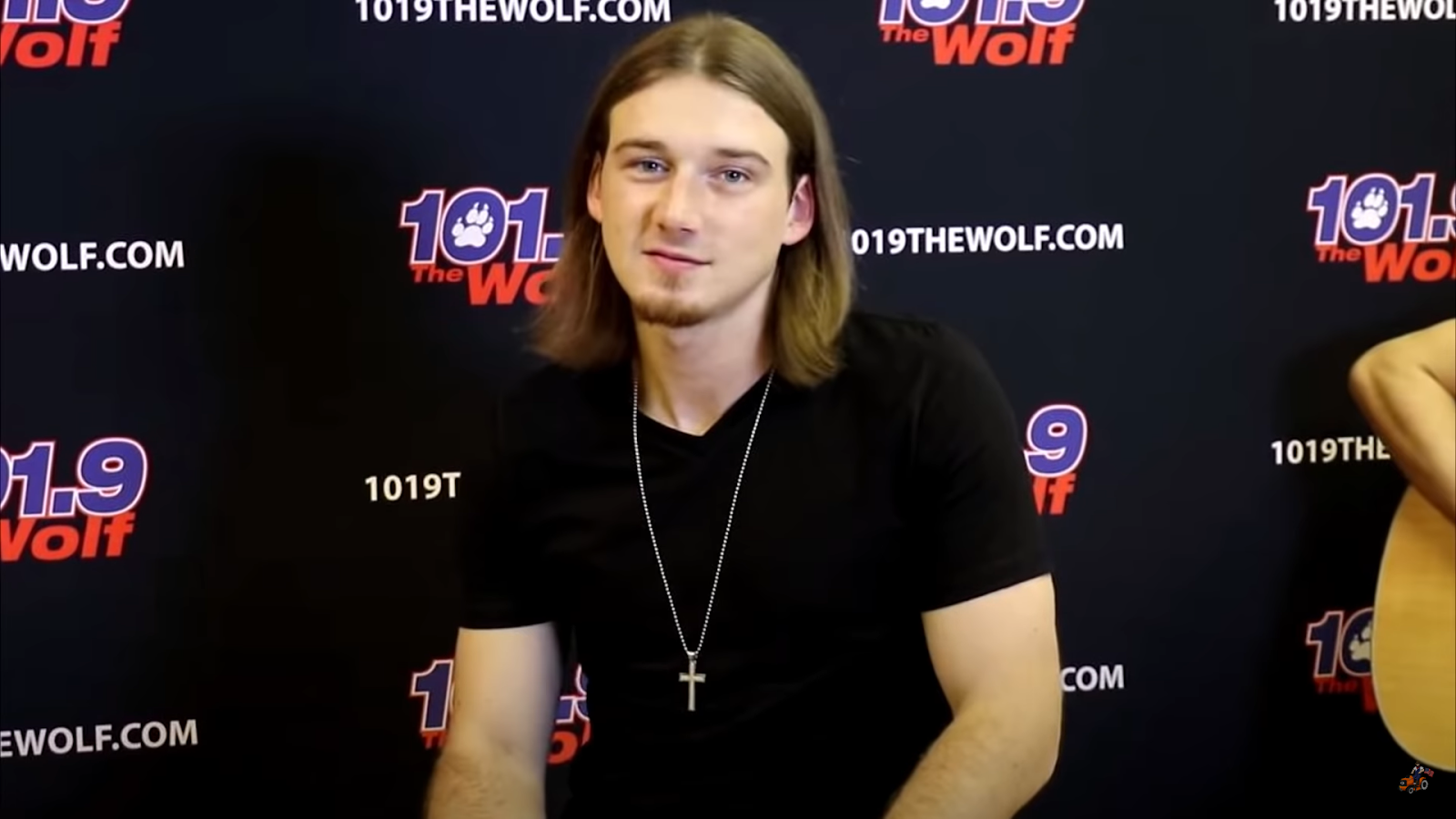 morgan wallen in a black T-shirt sitting in front of the wall with 101.09 the wolf poster