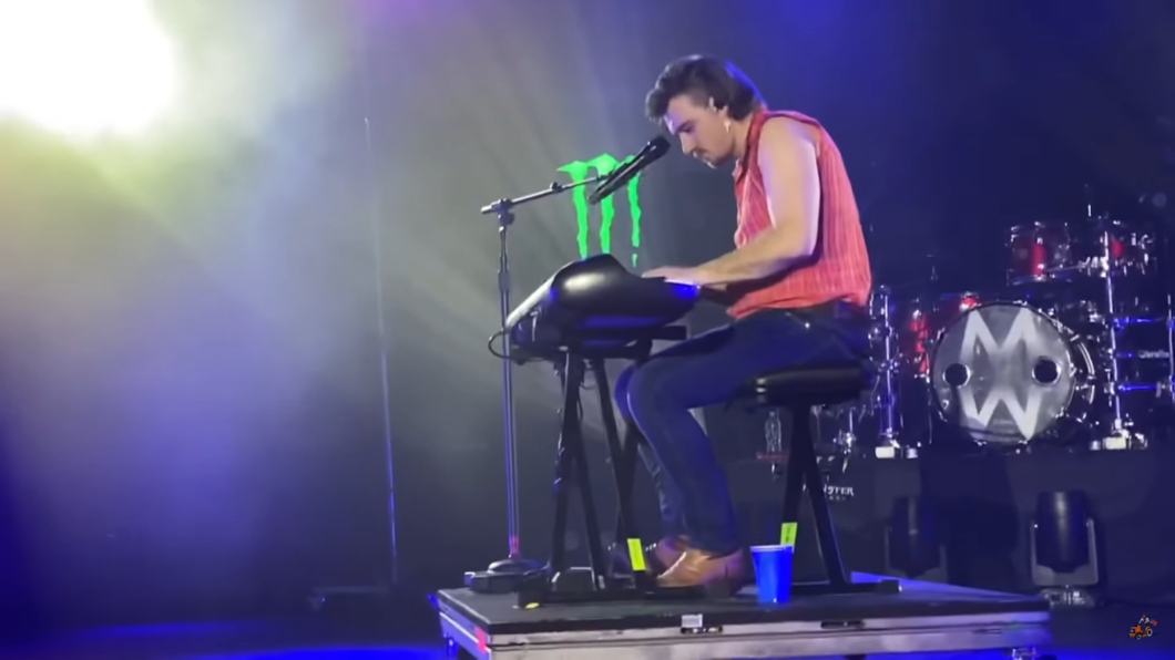 Morgan Wallen sitting in a  chair on the stage, the drums behind him