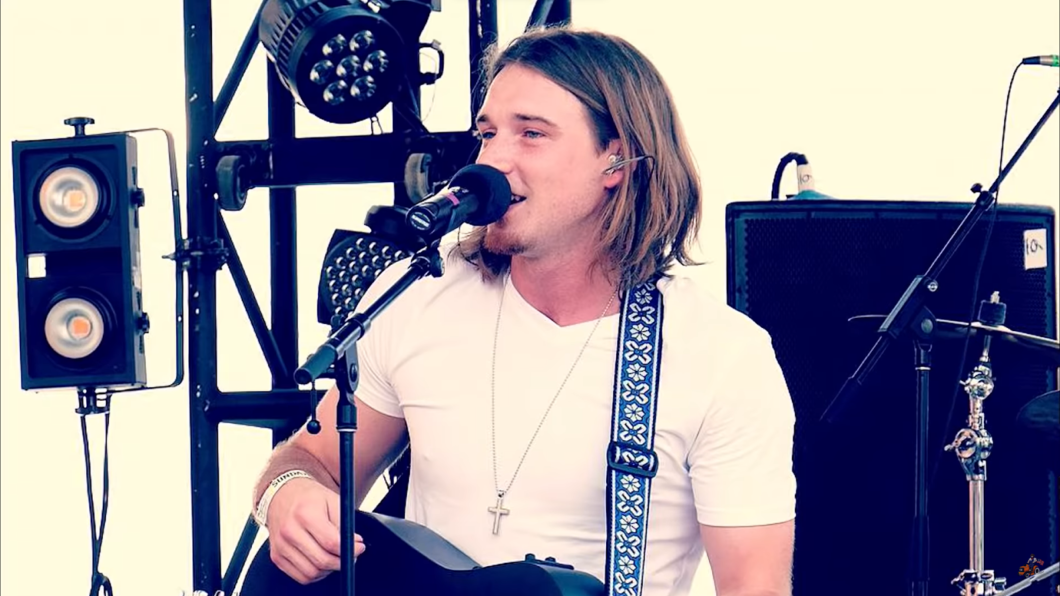 morgan wallen standing on the stage near the microphone with guitar and singing