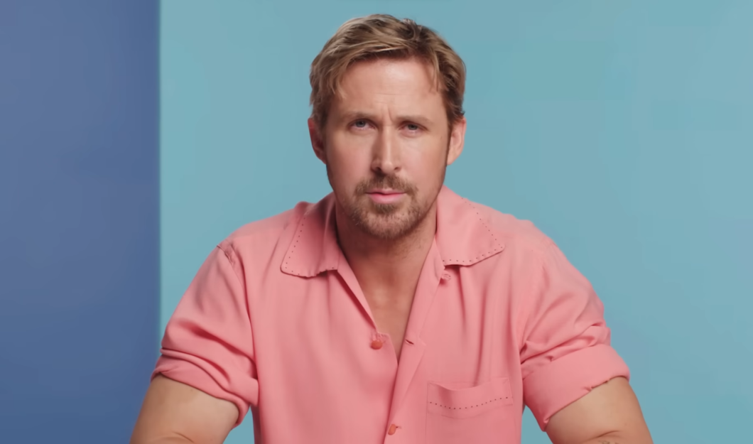 ryan gosling in a pink t-shirt sitting in front of the blue and turquoise wall