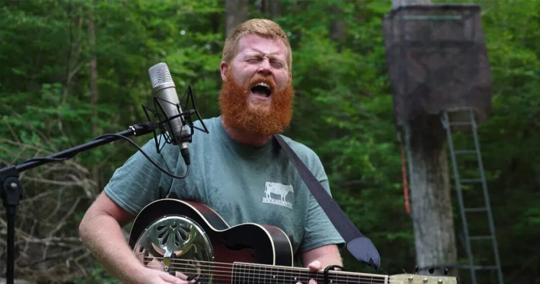 A man with a red beard sings and plays guitar