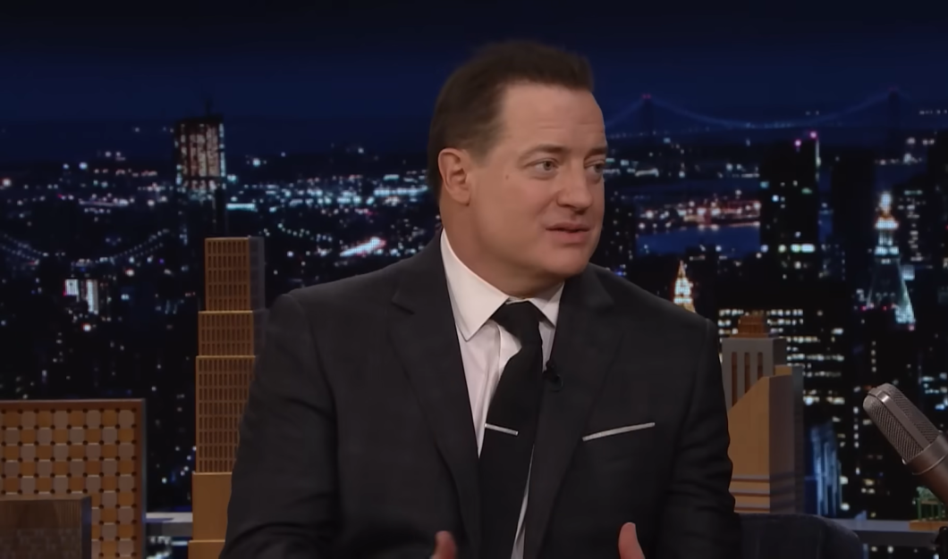 Brendan Fraser in a black suit and white shirt, the wall with picture of the city at night
