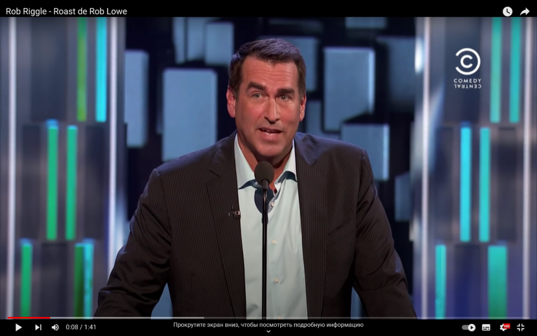Rob Riggle performs in front of a microphone in a suit